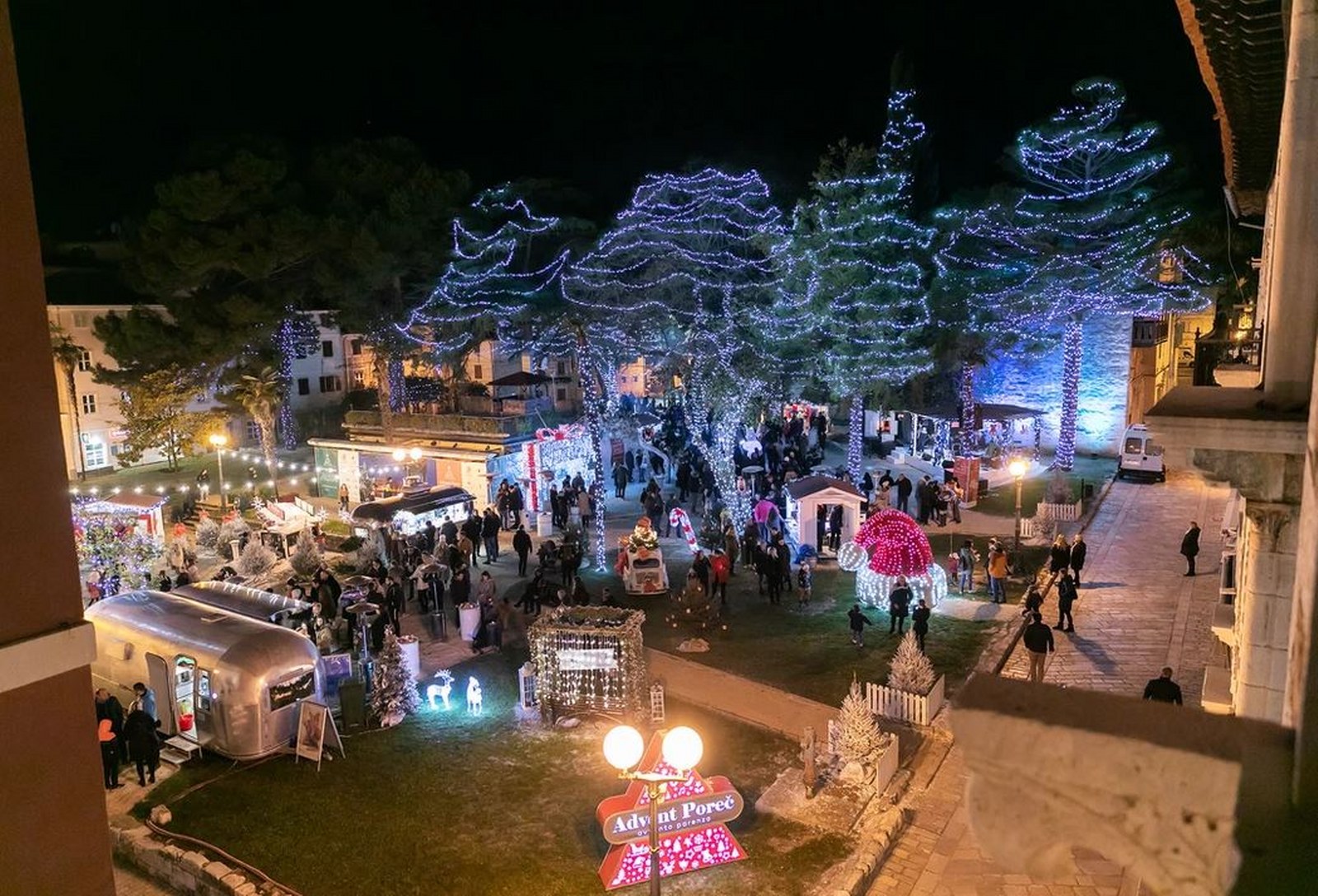 Advent Poreč Christmas market at night with light-draped trees and food stalls in Istria, Croatia.
