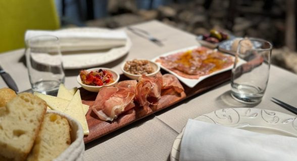 Rustic wooden platter with prosciutto, cheese and bread on a table set for lunch at Alavia Soulfood