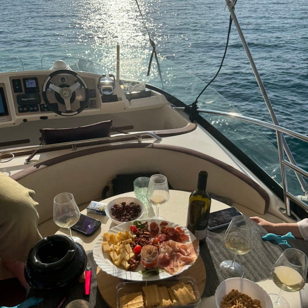 Charcuterie, wine and snacks on cockpit table with helm and glittering sea at sunset. 