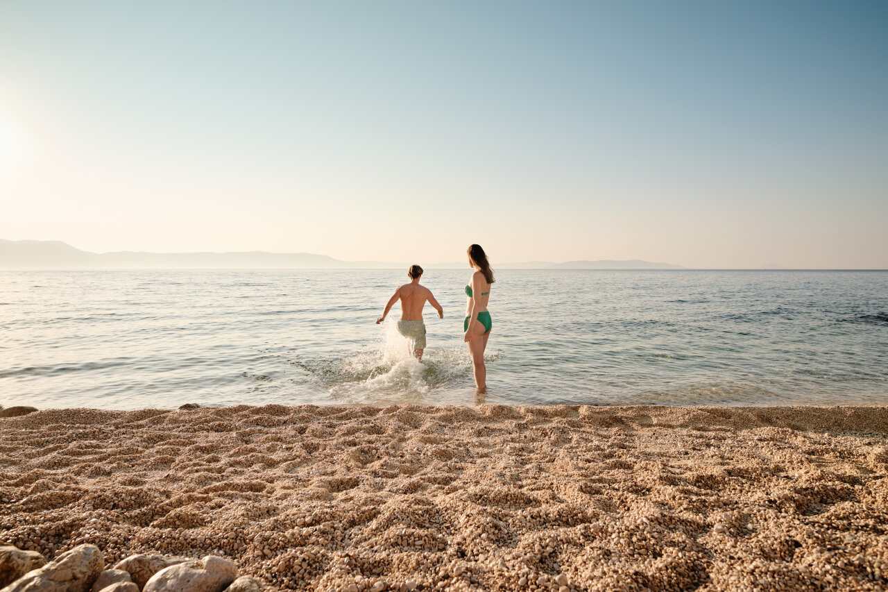 Couple entering the sea from a pebbly beach in Rabac Couple entering the sea from a pebbly beach in Rabac