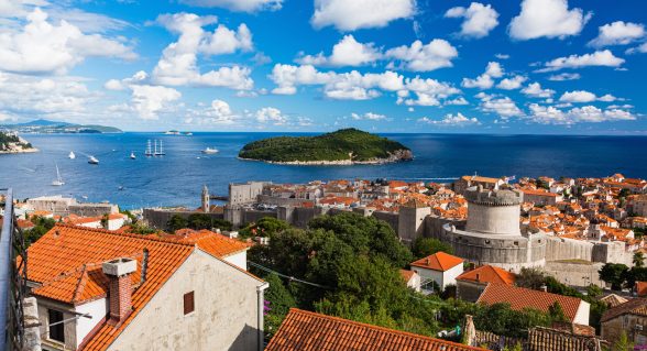 View of Lokrum Island from Dubrovnik’s Old Town, with terracotta rooftops, medieval city walls, and the Adriatic Sea in the background.