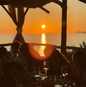 A group of people having a painting workshop by the sea in Dubrovnik at sunset, with the sun reflecting over the Adriatic horizon.