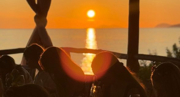 A group of people having a painting workshop by the sea in Dubrovnik at sunset, with the sun reflecting over the Adriatic horizon.