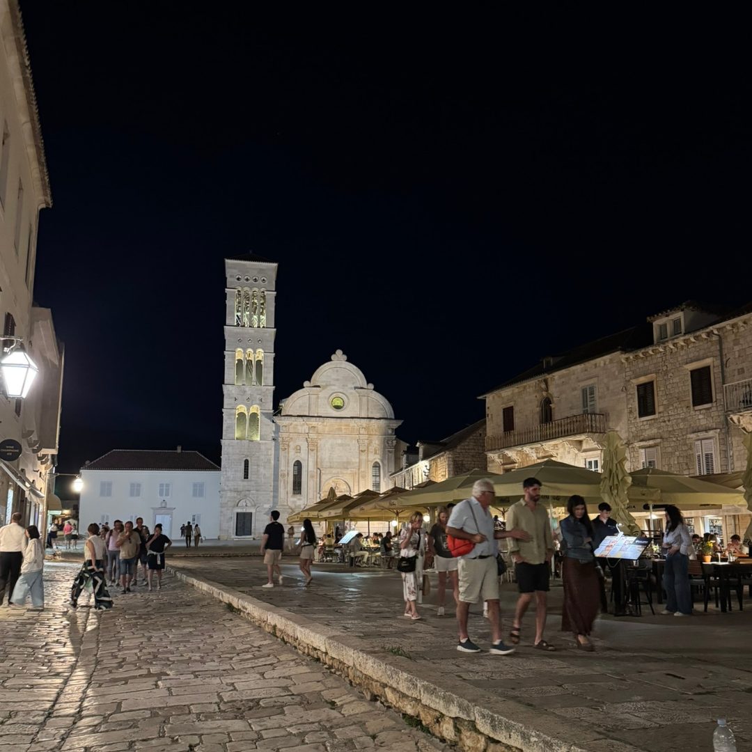 St. Stephen&rsquo;s Cathedral illuminated at night in Hvar Town, with people walking across the stone-paved main square.