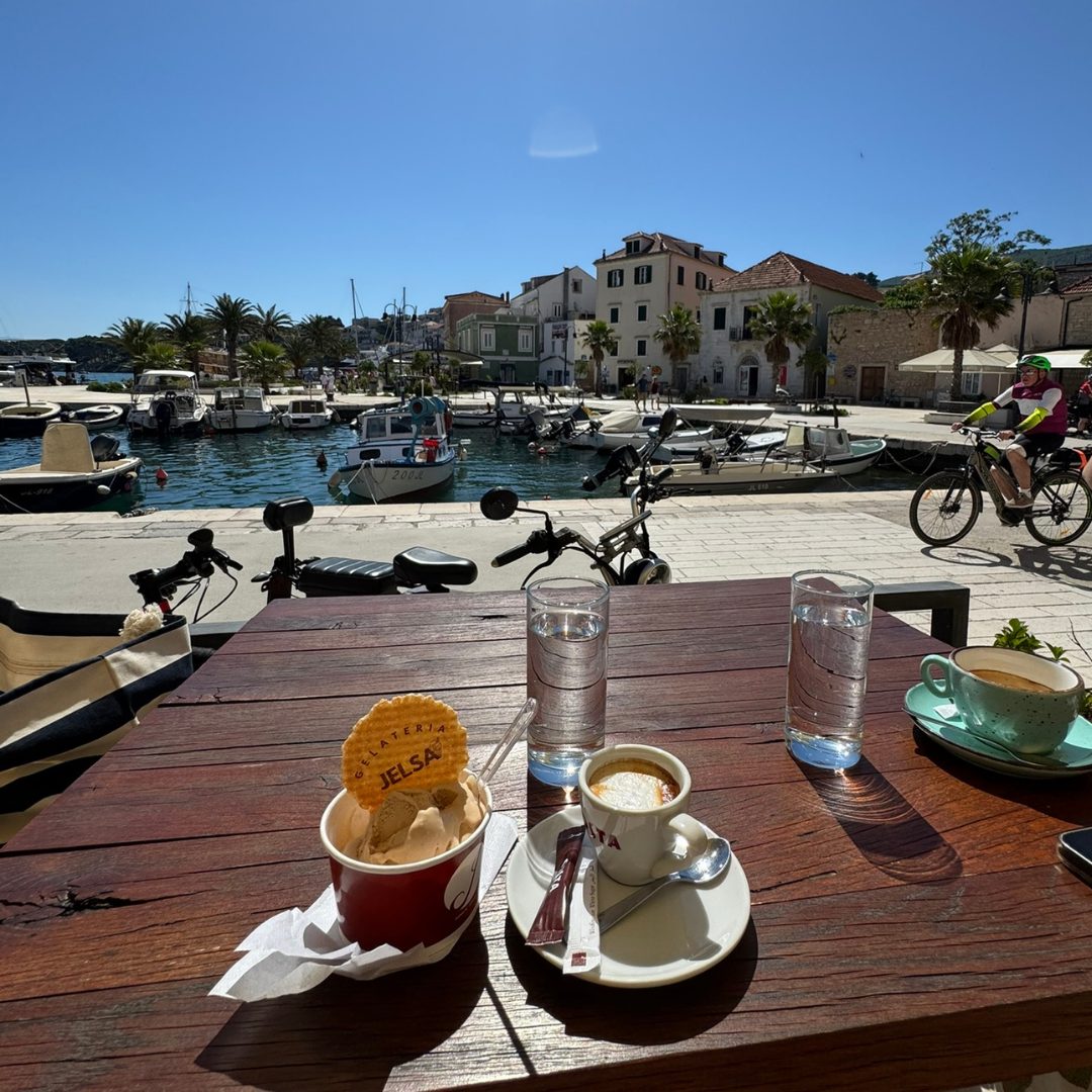 Coffee and gelato are served at a waterfront caf&eacute; in Jelsa, with boats docked in the harbour and colourful houses in the background.