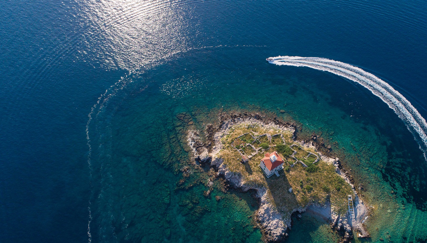 Motorboat cruising around a small island with a lighthouse near the coast of Cres