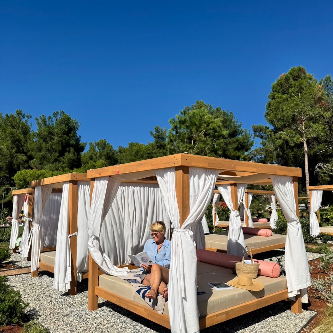 A person is relaxing on a shaded cabana bed with white curtains, reading a magazine. A person is relaxing on a shaded cabana bed with white curtains, reading a magazine.