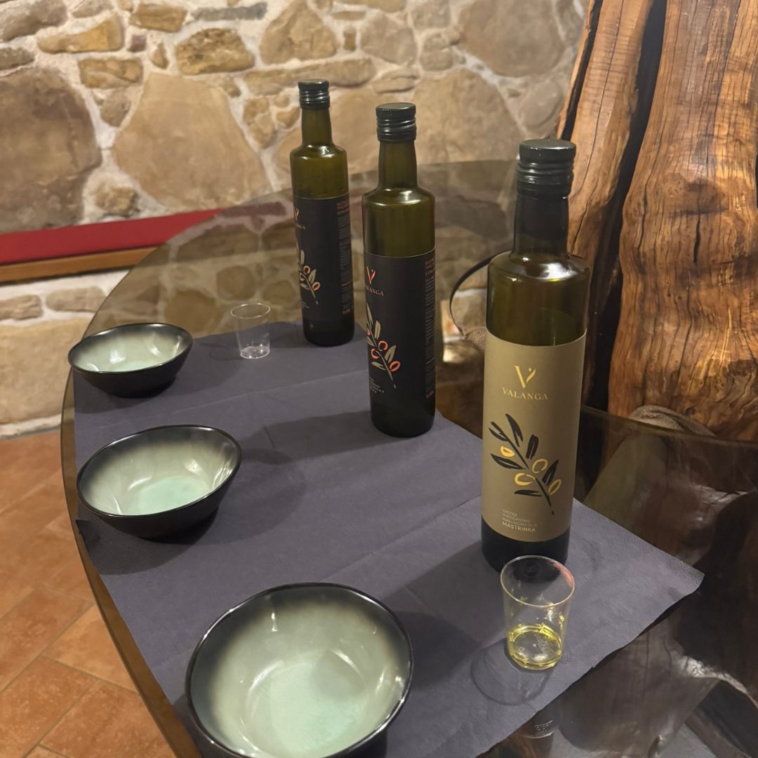 Bottles of Valanga olive oil with tasting bowls and glasses set on a rustic wooden table. Bottles of Valanga olive oil with tasting bowls and glasses set on a rustic wooden table.