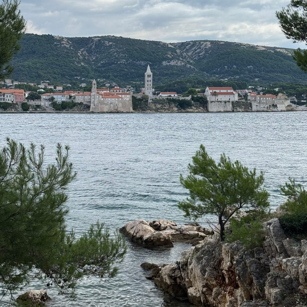 Scenic view of Rab’s old town with its historic bell towers, seen across the sea from a rocky pine-fringed coastline of the peninsula of Frkanj. Scenic view of Rab’s old town with its historic bell towers, seen across the sea from a rocky pine-fringed coastline of the peninsula of Frkanj.