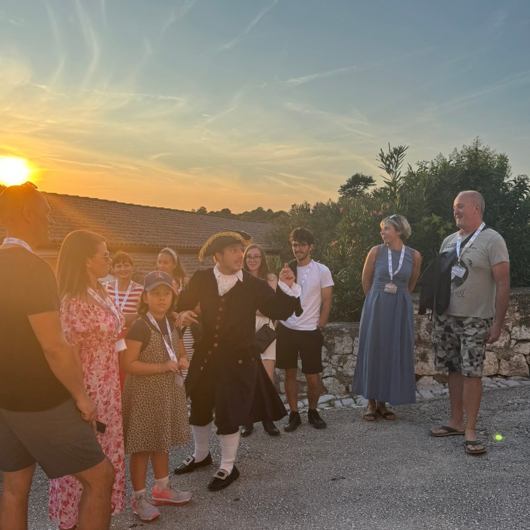 Guided by Don Gerolamo, visitors explore Vrsar with laughter and curiosity. Actor portraying Don Gerolamo leading a group of visitors through Vrsar at sunset.