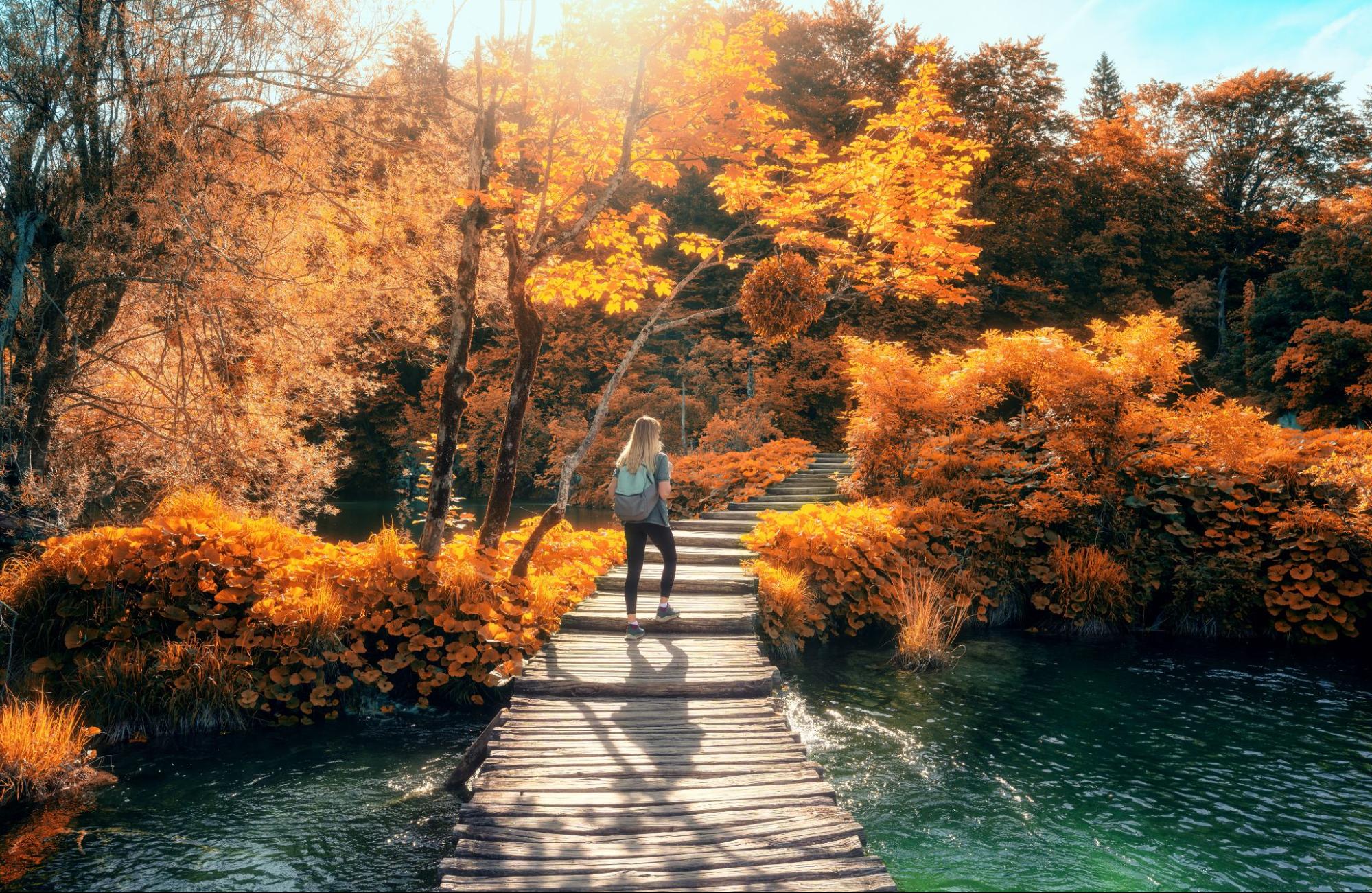 Eine Frau läuft im Oktober durch den Nationalpark Plitvicer Seen in Kroatien, umgeben von Herbstfarben Eine Frau läuft im Oktober durch den Nationalpark Plitvicer Seen in Kroatien, umgeben von Herbstfarben