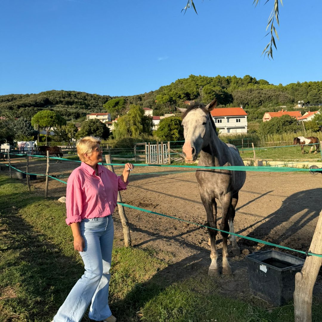 Woman standing beside a horse at Soline Ranch on Rab Island, surrounded by greenery and stables. Woman standing beside a horse at Soline Ranch on Rab Island, surrounded by greenery and stables.