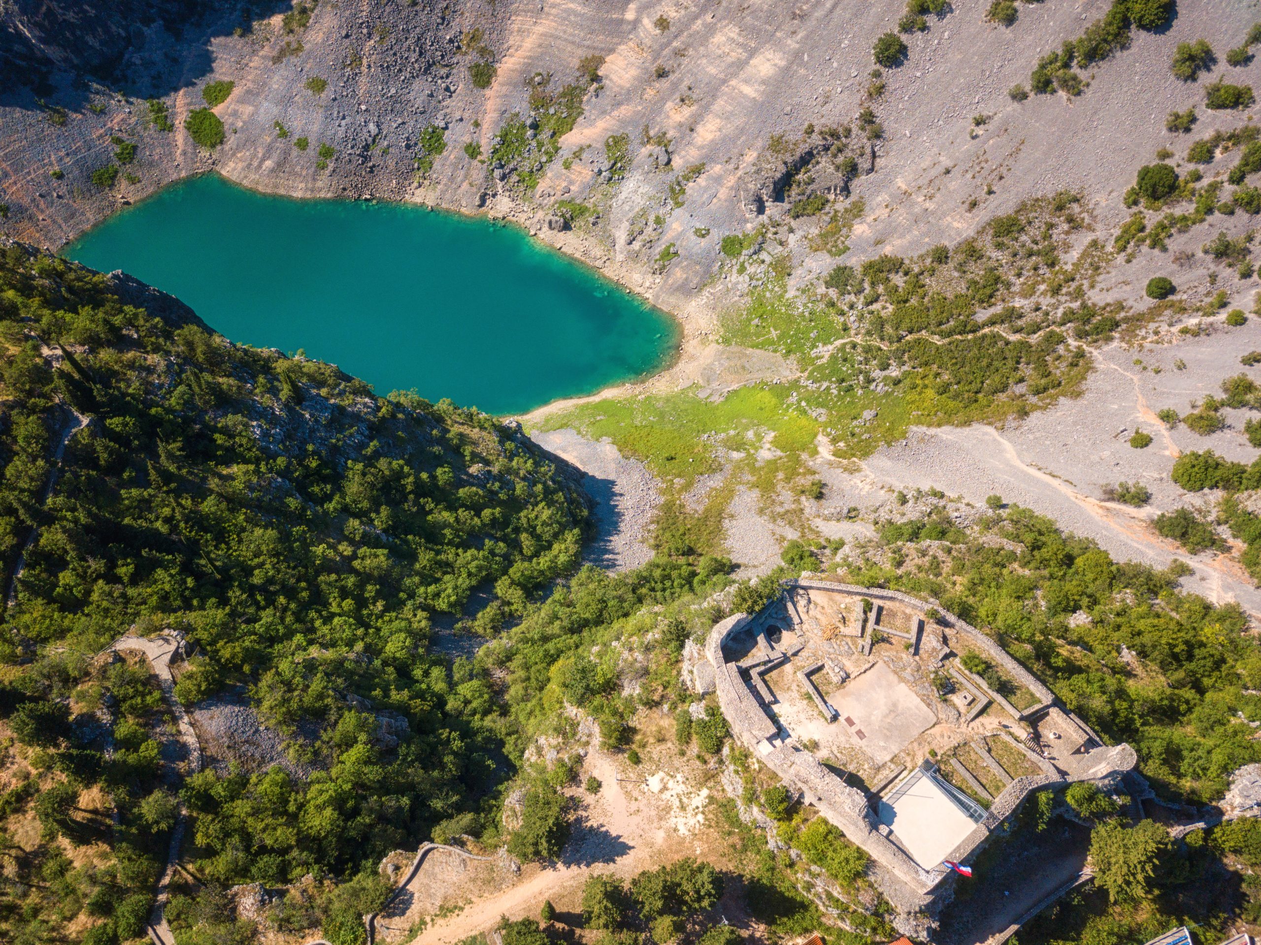 Aerial view of the Blue Lake (Modro jezero) in Imotski with turquoise water and nearby fortress ruins. Aerial view of the Blue Lake (Modro jezero) in Imotski with turquoise water and nearby fortress ruins.
