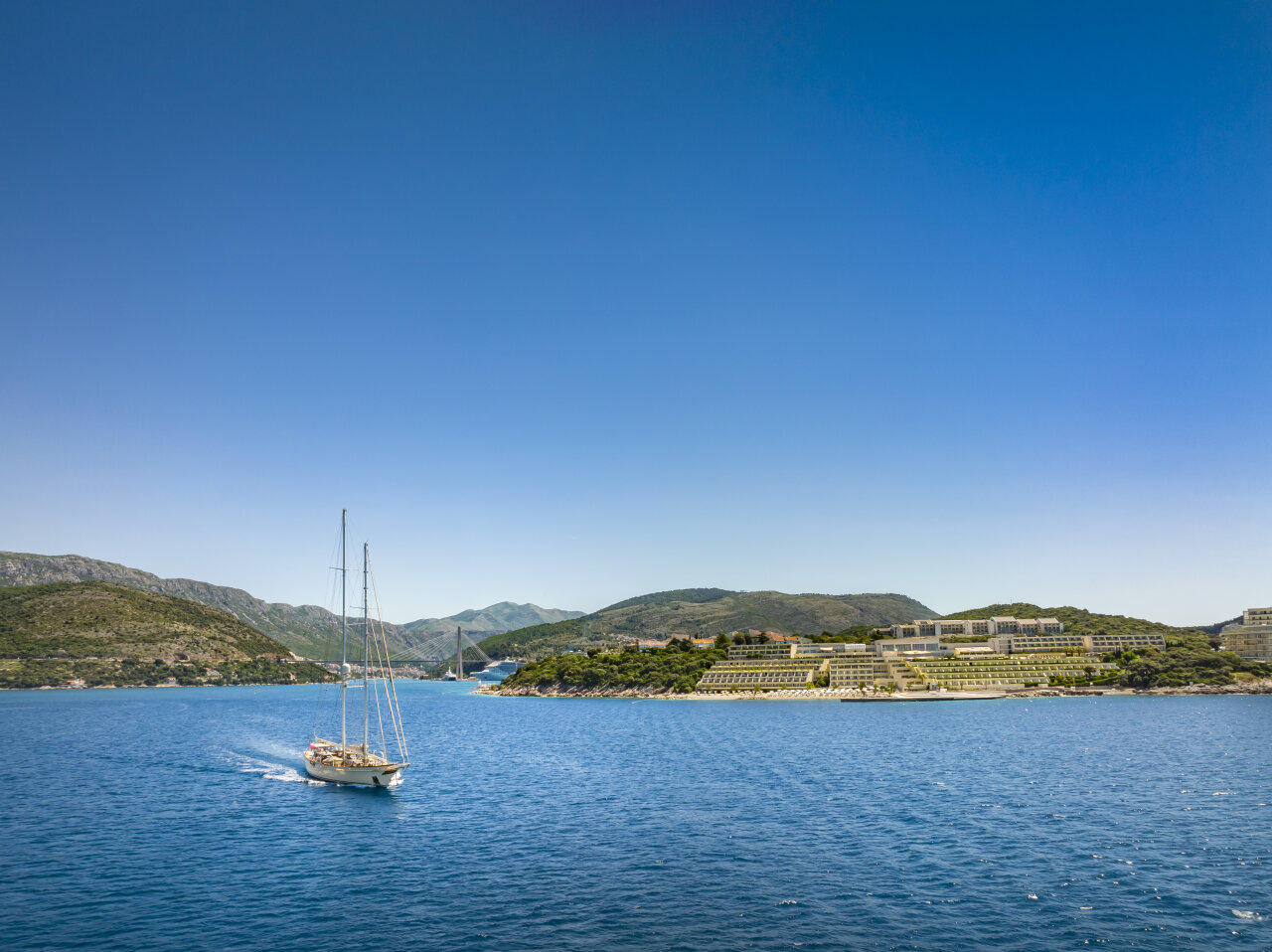 Sailboat on the Adriatic passing Babin Kuk with the Valamar Collection Dubrovnik President Hotel on the shoreline and the Franjo Tuđman Bridge in the distance.