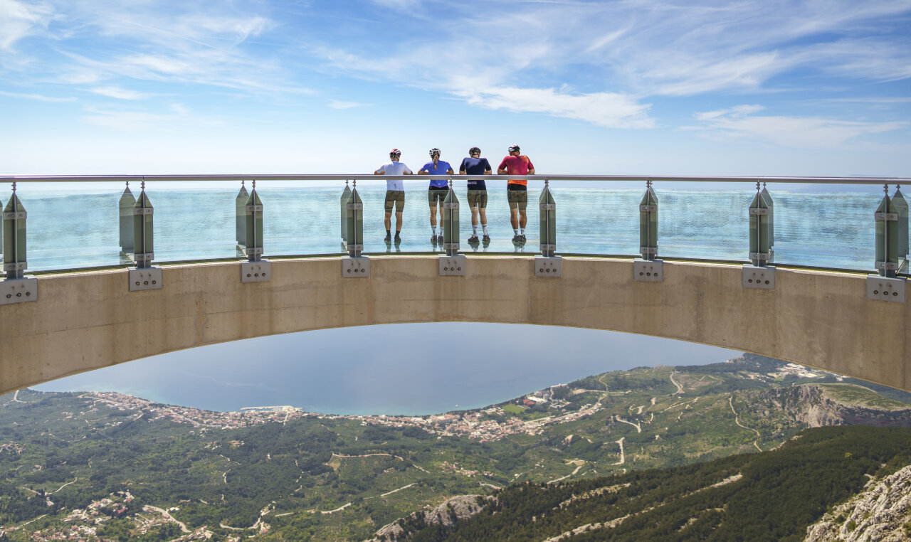 Cyclists standing on the Biokovo Skywalk glass viewpoint above the Makarska Riviera, gazing over the Adriatic. 