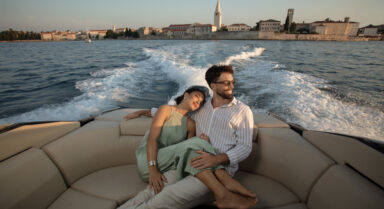 A couple relaxes on a luxury boat during sunset, with the historic coastal town of Poreč.