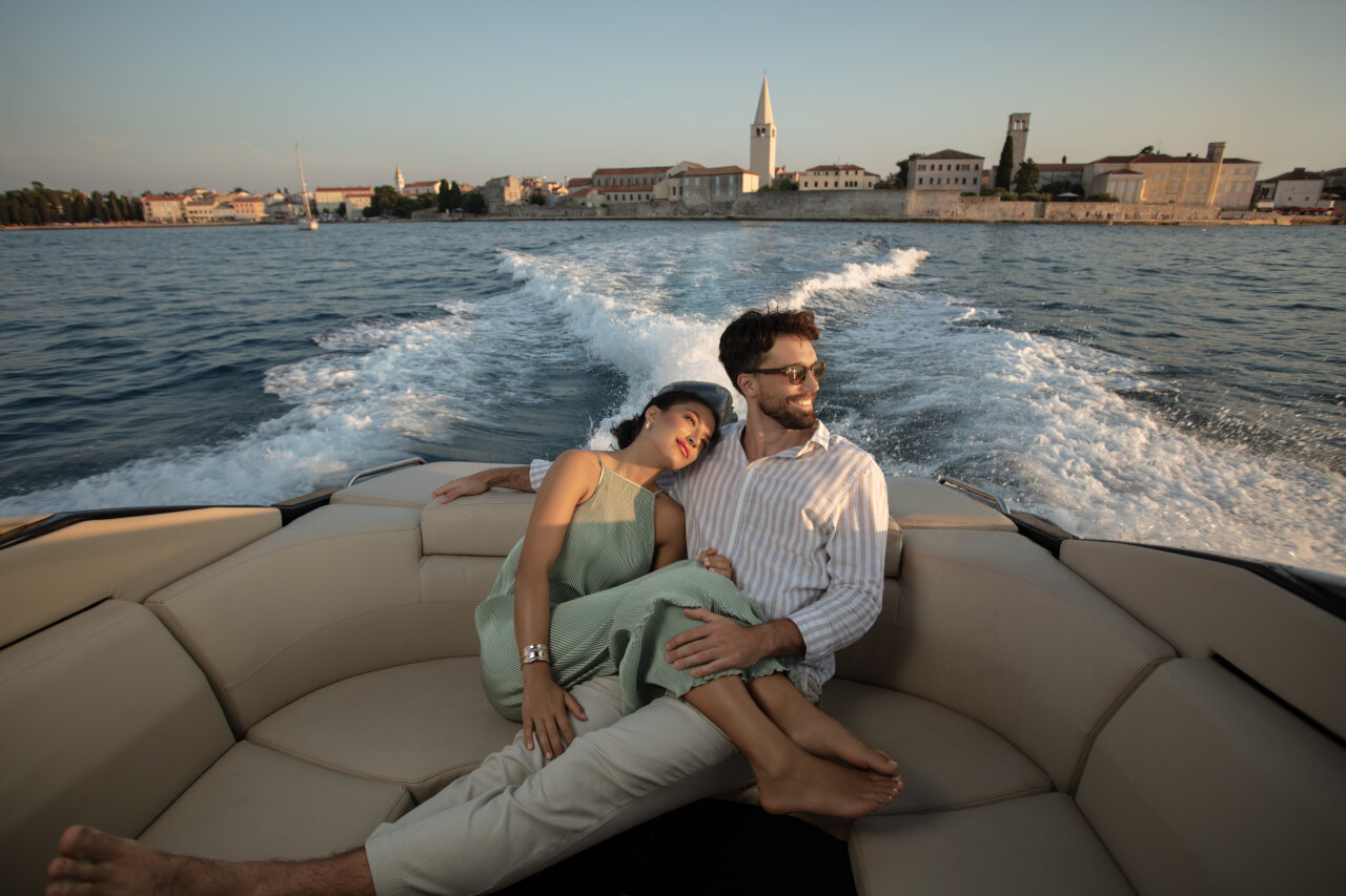 A couple relaxes on a luxury boat during sunset, with the historic coastal town of Poreč. A couple relaxes on a luxury boat during sunset, with the historic coastal town of Poreč.