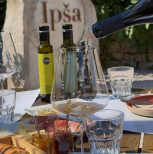 Close-up of a tasting table at Ipša with extra virgin olive oils, bread, cheeses, charcuterie, jams, and white wine being poured.