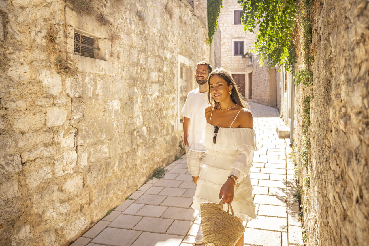 A smiling couple walks through a narrow stone alleyway in Stari Grad on a sunny day. A smiling couple walks through a narrow stone alleyway in Stari Grad on a sunny day.