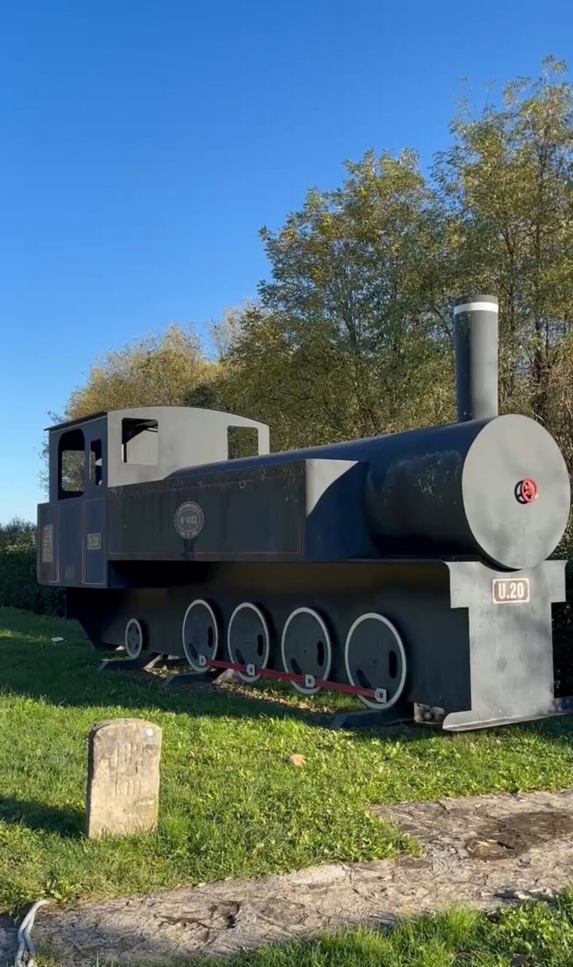 Parenzana steam-locomotive memorial with five driving wheels on a grassy verge.