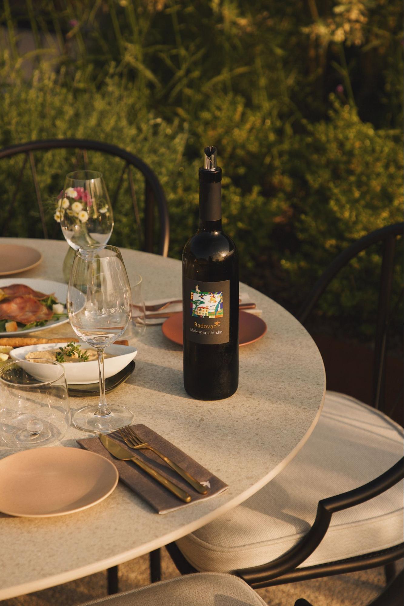 Ein gedeckter Tisch im Freien mit einer Flasche Rotwein, Gläsern und Tellern. Ein gedeckter Tisch im Freien mit einer Flasche Rotwein, Gläsern und Tellern.