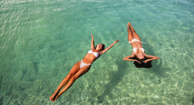 Two women floating on their backs in clear turquoise sea water on a sunny day