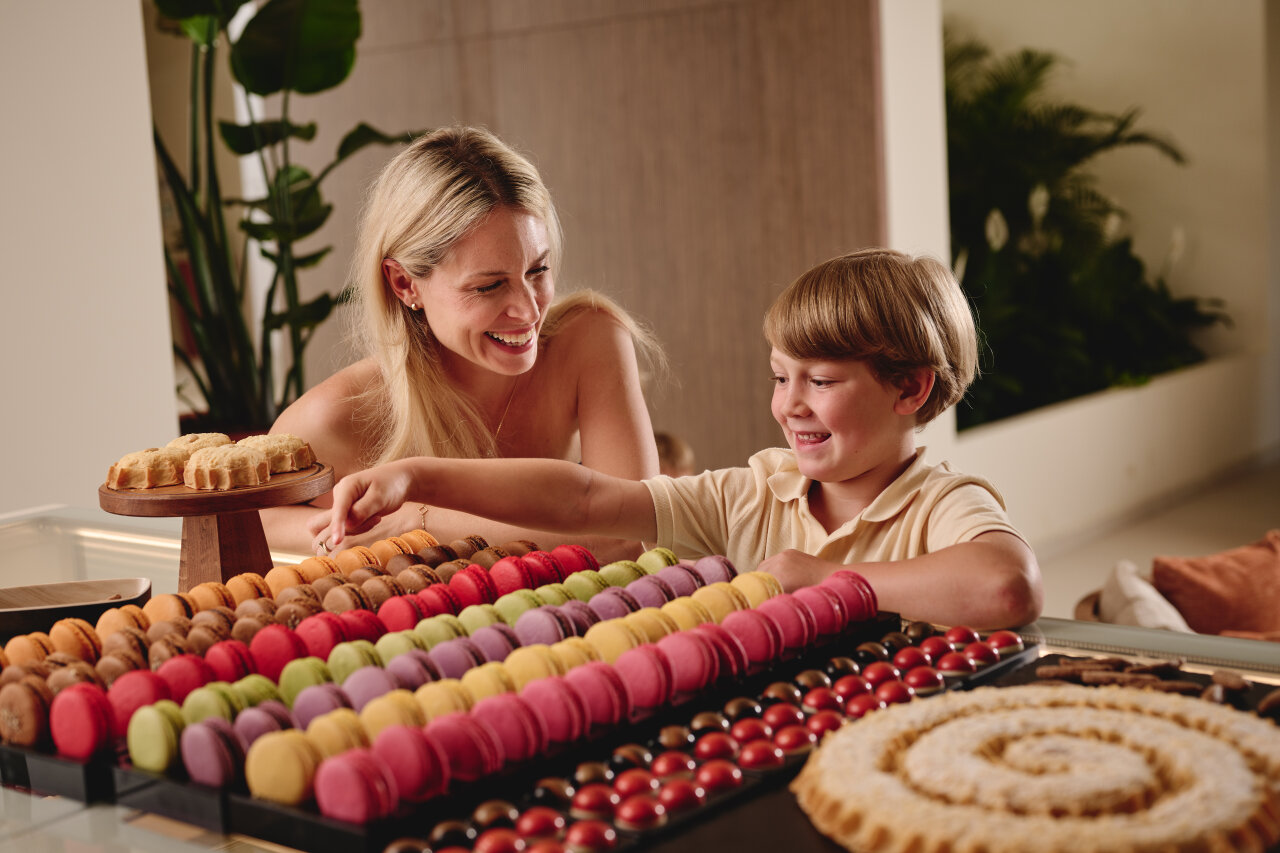 An adult and a child smile while choosing from a colourful display of macarons and pastries at Arba Resort. 