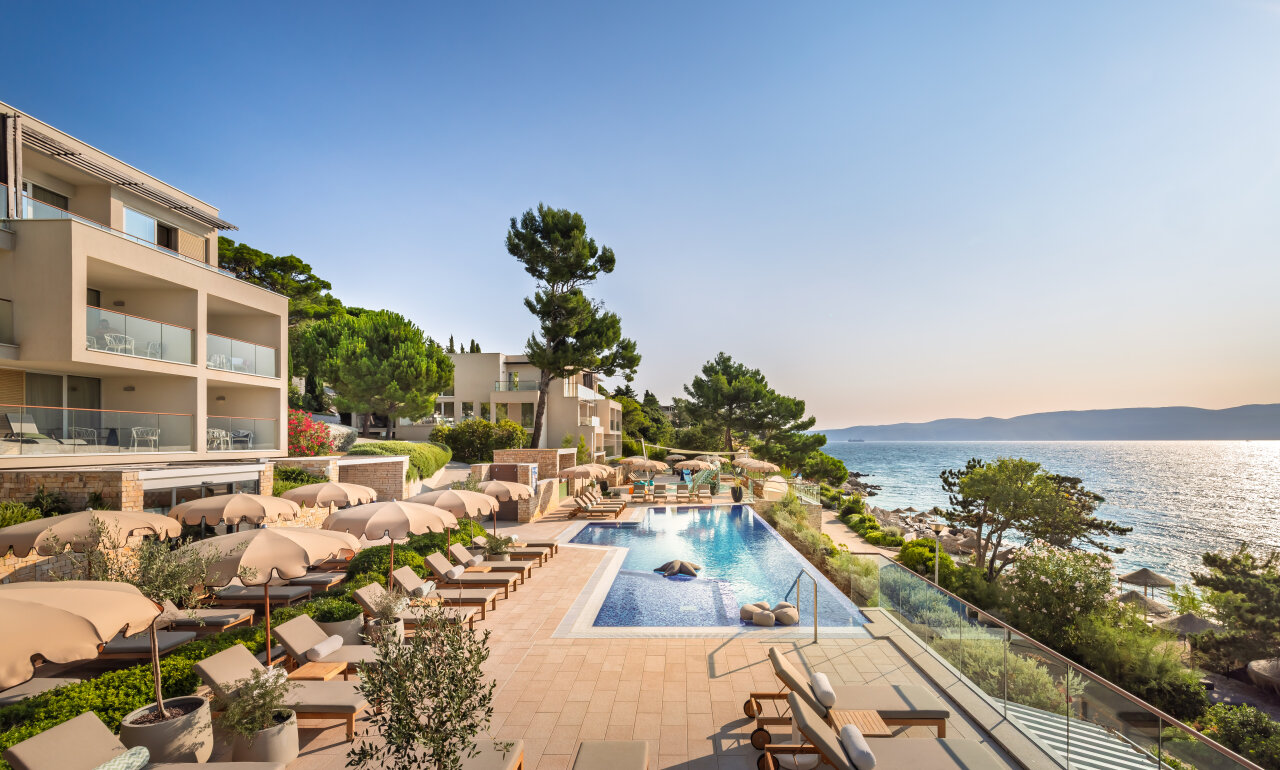A large outdoor pool with lounge chairs and umbrellas overlooks the Adriatic Sea in Rabac.