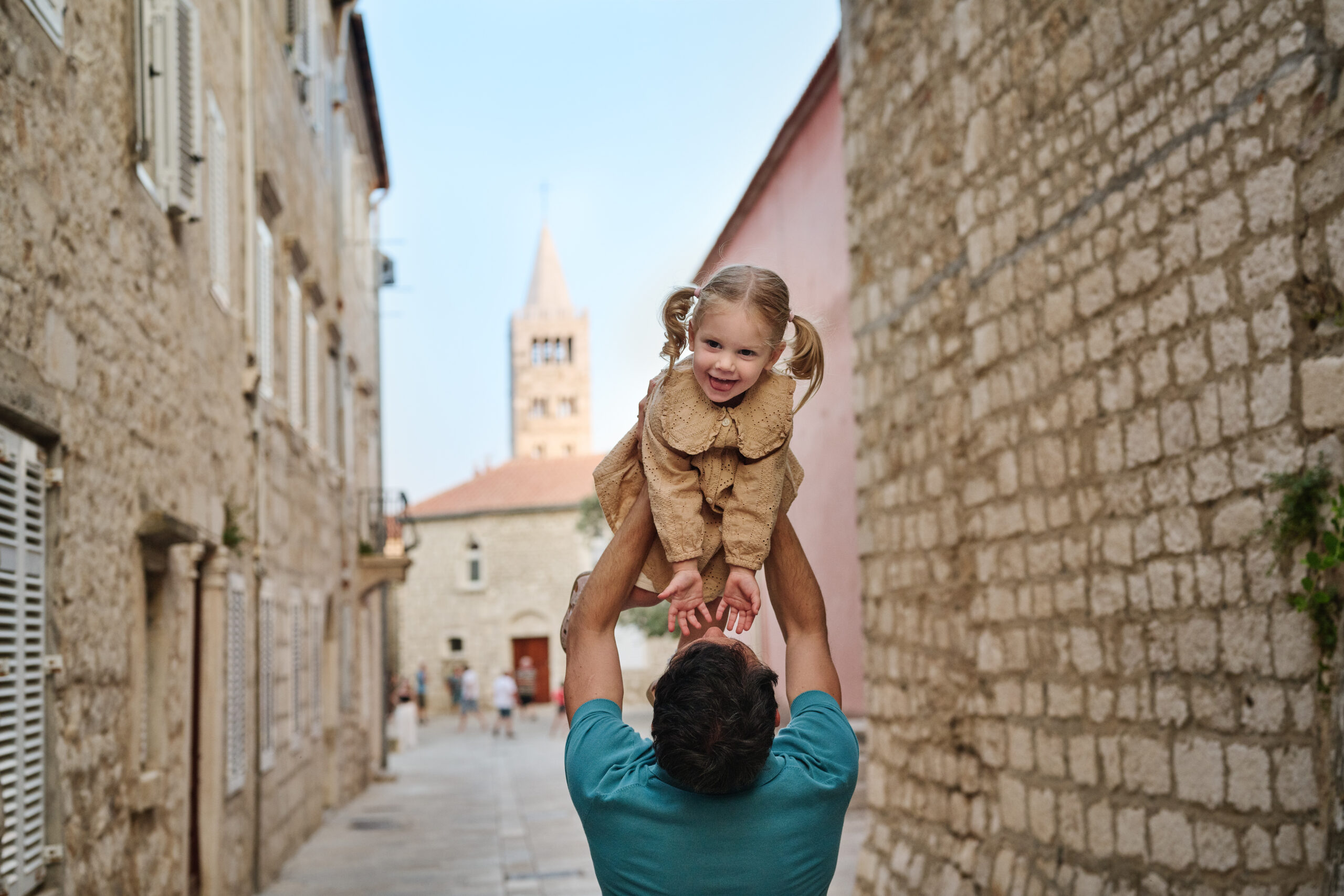 Family moment in a stone street of Rab Town with a church tower in the background
