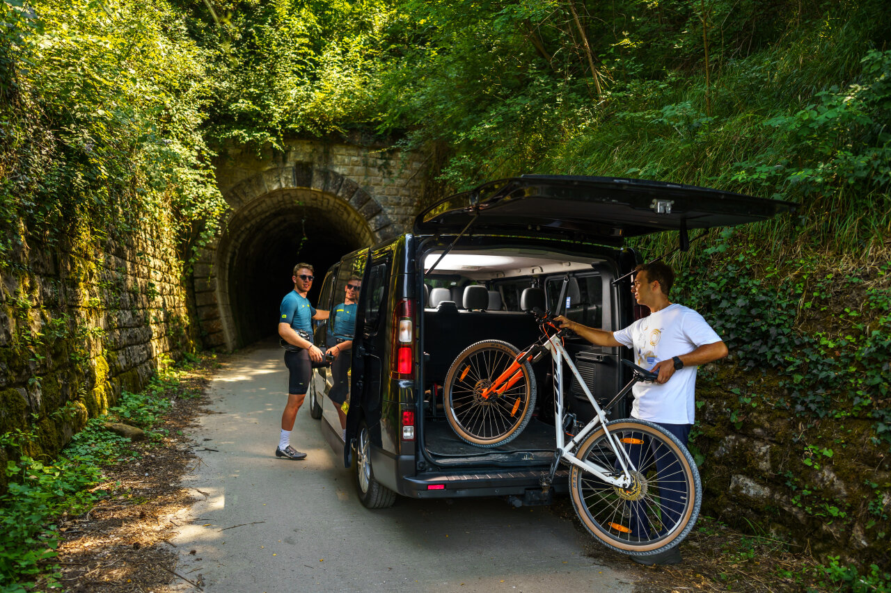 A man unloading bikes from a support van at the entrance of a forest tunnel on a scenic cycling route in Istria.