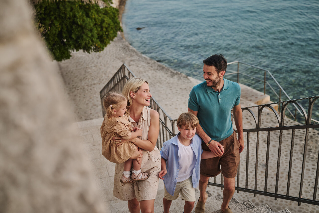 A family with two children climbing stone steps by the sea during a walk along the coast of Rab Town.