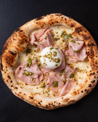 Mortadella and pistachio pizza served on a dark surface