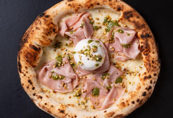 Mortadella and pistachio pizza served on a dark surface