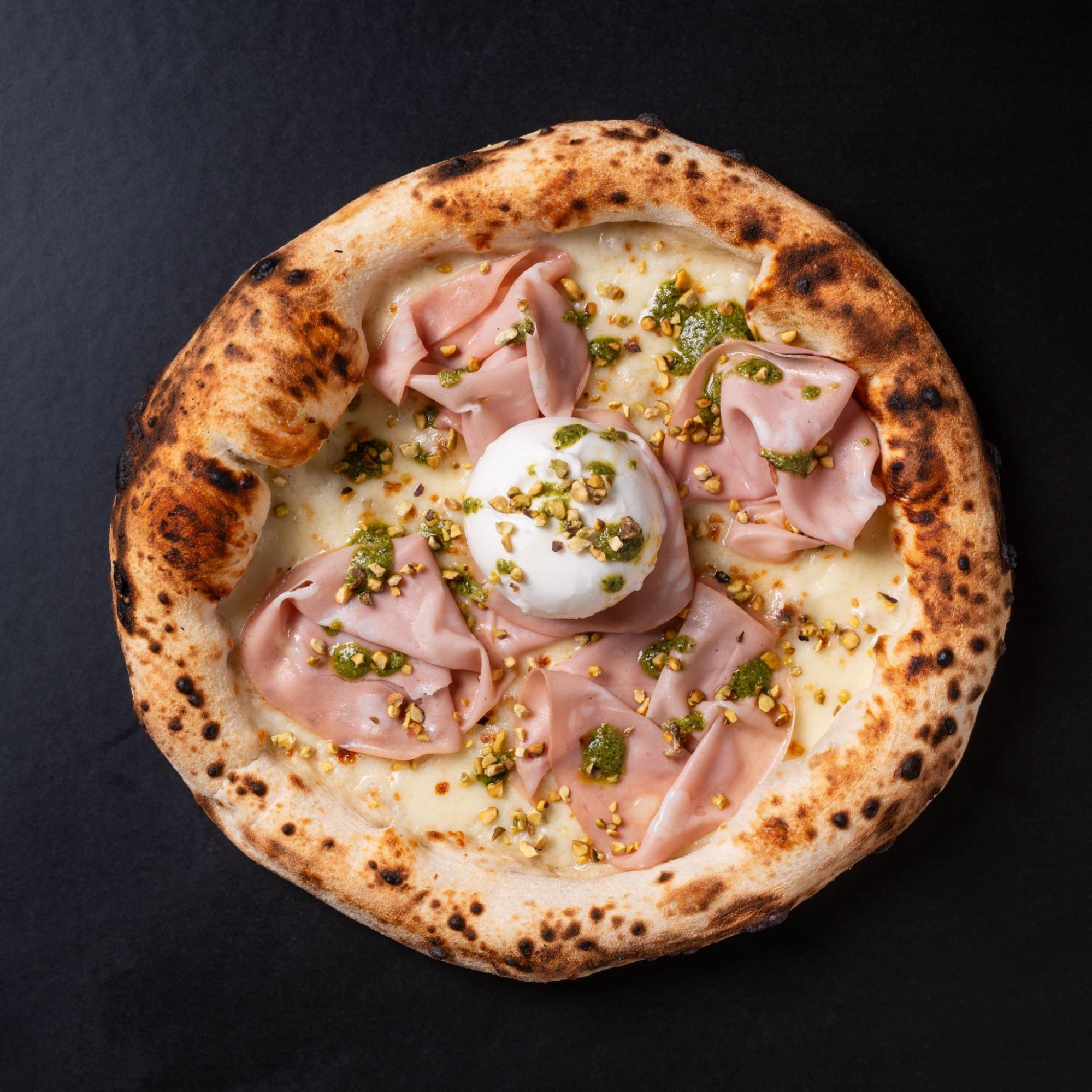 Mortadella and pistachio pizza served on a dark surface