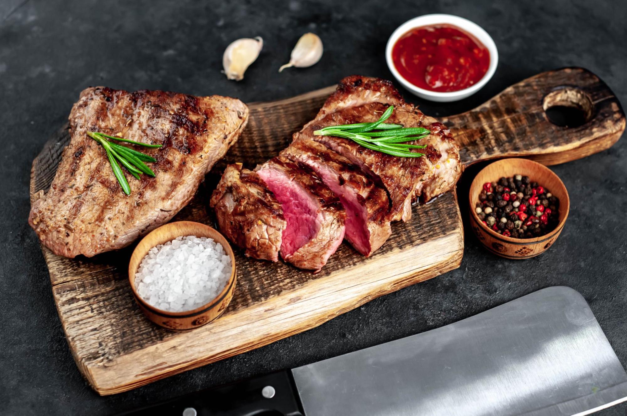 Two beautifully plated steaks served on a wooden board with herbs and seasoning