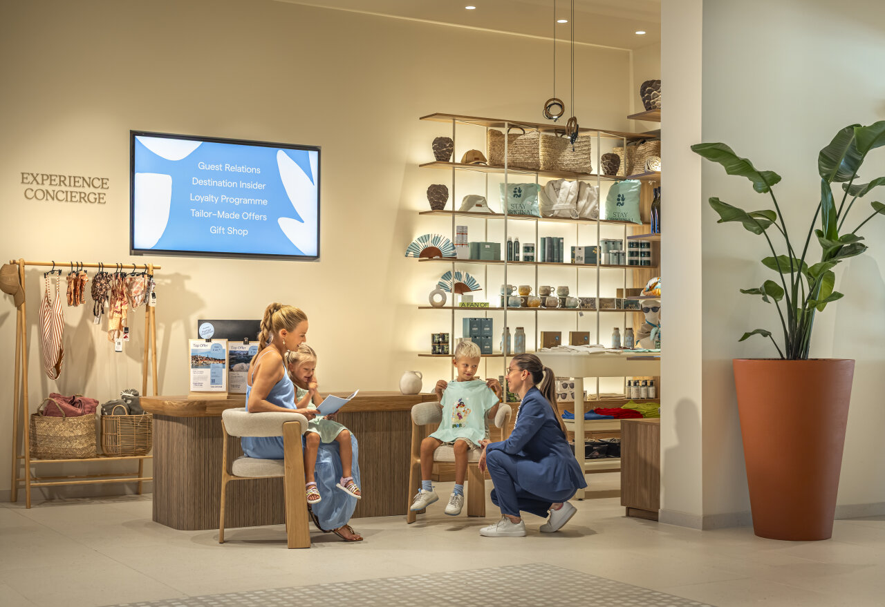 A mother with children speaking to an Experience Concierge staff member in a hotel area with offers for guests and families.