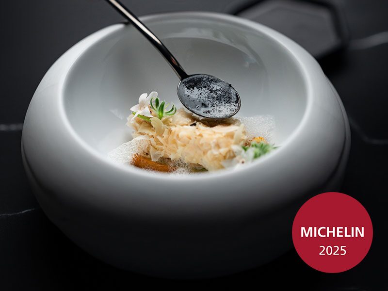 Creatively plated gourmet dish in a white bowl, with carefully arranged ingredients and a Michelin 2025 label