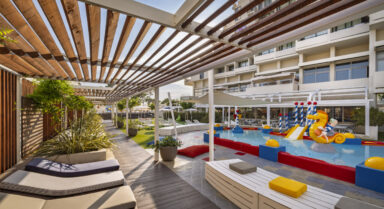 An outdoor children’s pool with slides, sprinklers and a relaxation area in a family resort.