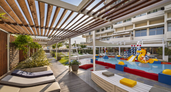 An outdoor children’s pool with slides, sprinklers and a relaxation area in a family resort.