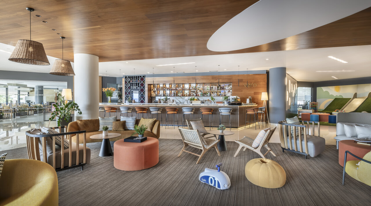 A modern hotel lounge with comfortable seating, a bar and a children&rsquo;s corner in the background.