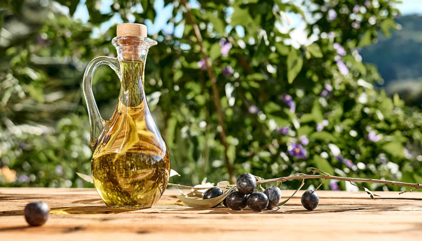 Bottle of olive oil and fresh olives on a wooden table in a garden setting&nbsp;