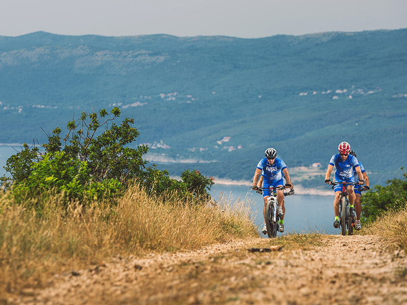 A group of people cycling on a gravel road near Rabac with a sea view in the background.